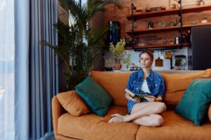 Cozy reading corner with woman on orange couch, book in front, and plant in background